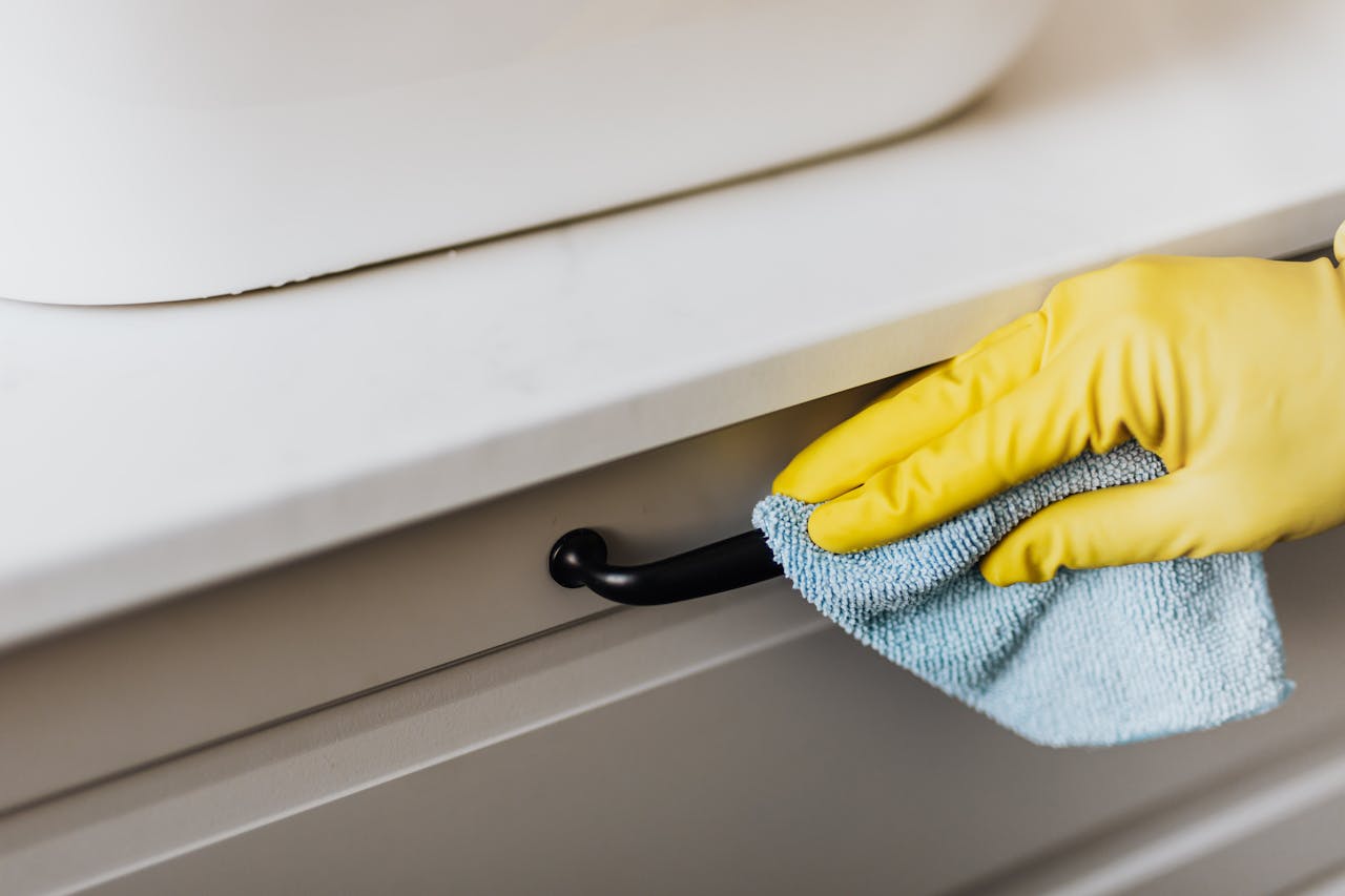 why-choose-us-03 From above of crop faceless person in yellow gloves cleaning handle of cabinet with microfiber cloth in modern bright bathroom